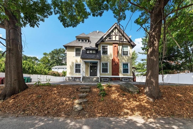 victorian house with stucco siding, roof with shingles, and fence