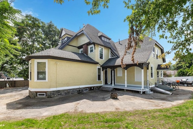 view of front of property featuring roof with shingles, stucco siding, covered porch, and fence