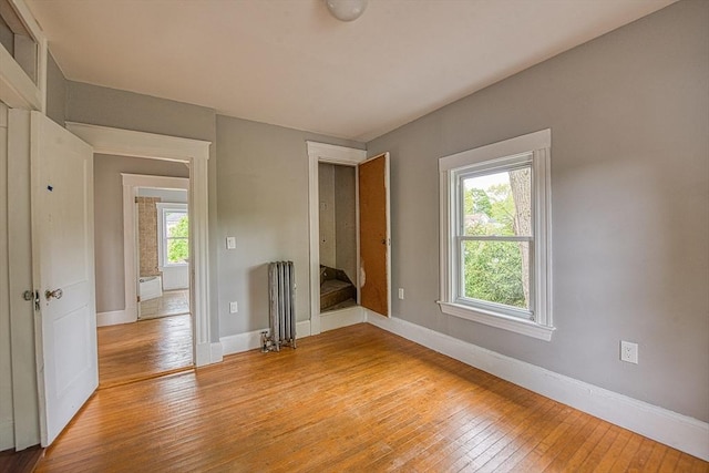 unfurnished room featuring radiator heating unit, light wood finished floors, and baseboards