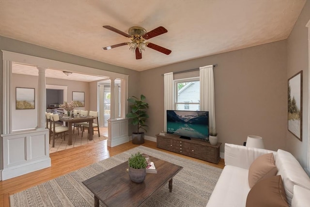 living area with ornate columns, a ceiling fan, light wood-style flooring, and baseboards