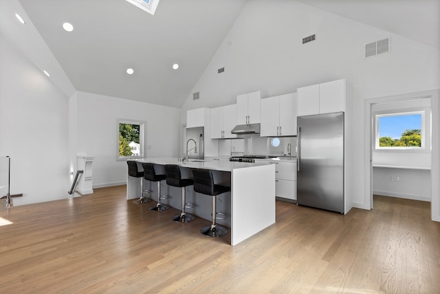 kitchen featuring high vaulted ceiling, built in fridge, a kitchen breakfast bar, a center island with sink, and white cabinets