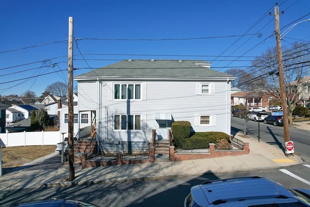 view of front of house with entry steps, a residential view, fence, and roof with shingles