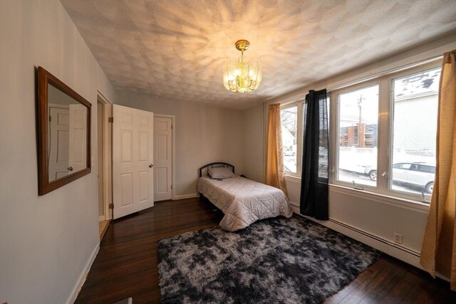 bedroom featuring baseboards, dark wood finished floors, an inviting chandelier, a textured ceiling, and a baseboard heating unit