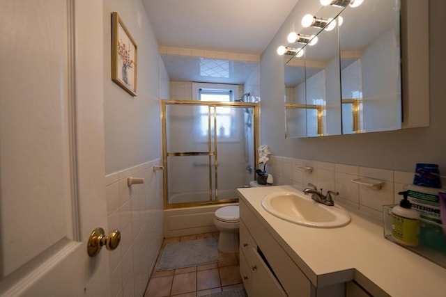 full bath with tile patterned flooring, toilet, bath / shower combo with glass door, vanity, and tile walls