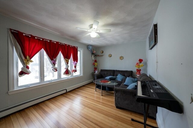 living area featuring light wood-style floors, a baseboard heating unit, ceiling fan, and a textured ceiling