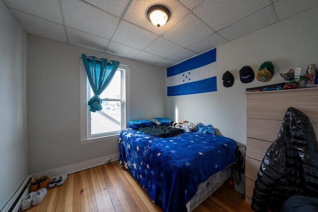 bedroom with hardwood / wood-style floors, a baseboard radiator, a paneled ceiling, and baseboards