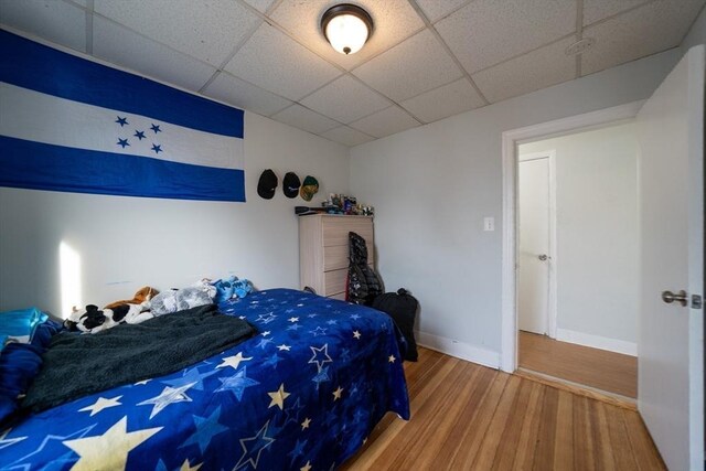 bedroom featuring baseboards, a drop ceiling, and wood finished floors