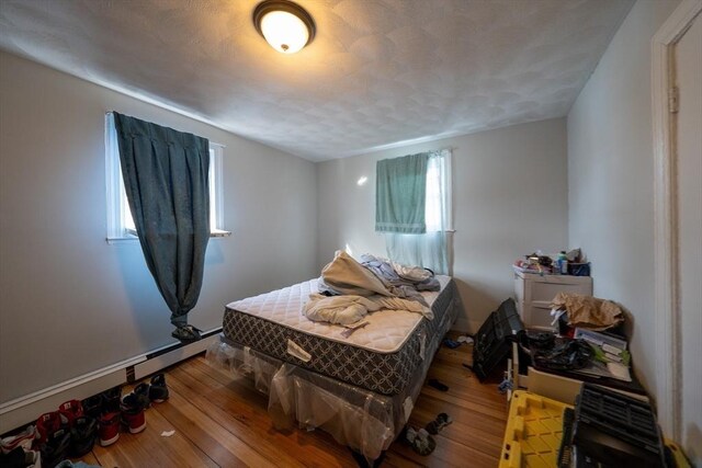 bedroom featuring a baseboard heating unit, a textured ceiling, and hardwood / wood-style flooring