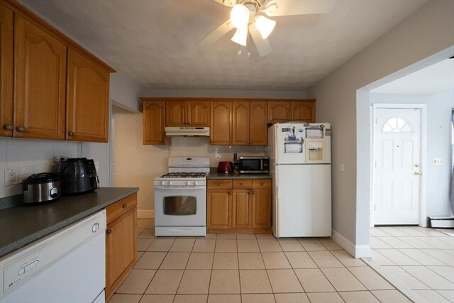 kitchen with brown cabinets, light tile patterned floors, decorative backsplash, white appliances, and under cabinet range hood