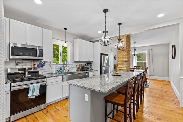 12 Russell St, Amesbury, MA 01913 - kitchen featuring stainless steel appliances, a center island, a kitchen breakfast bar, tasteful backsplash, and light wood-style floors