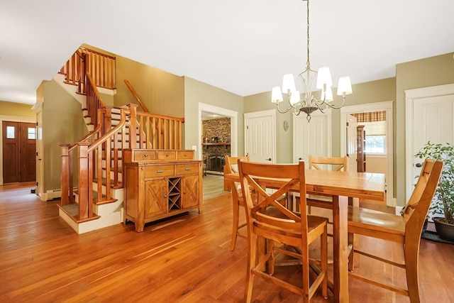 dining space with light hardwood / wood-style floors, a notable chandelier, and a stone fireplace