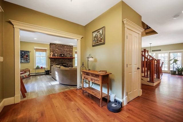 corridor featuring a healthy amount of sunlight, wood-type flooring, an inviting chandelier, and baseboard heating