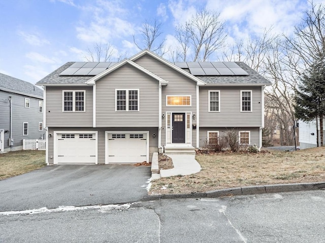 bi-level home with a front lawn, a garage, and solar panels