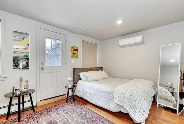 bedroom featuring an AC wall unit, a baseboard heating unit, light wood finished floors, and visible vents