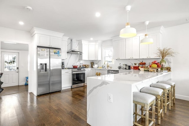 kitchen with dark wood finished floors, appliances with stainless steel finishes, a sink, wall chimney range hood, and a peninsula