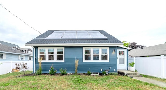 back of house with a shingled roof, fence, solar panels, and a yard