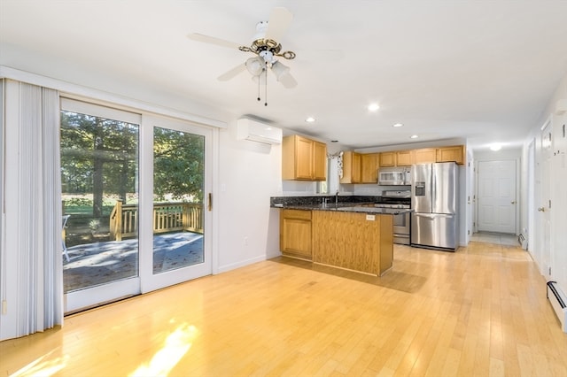 kitchen with kitchen peninsula, appliances with stainless steel finishes, dark stone counters, a wall mounted air conditioner, and light hardwood / wood-style floors