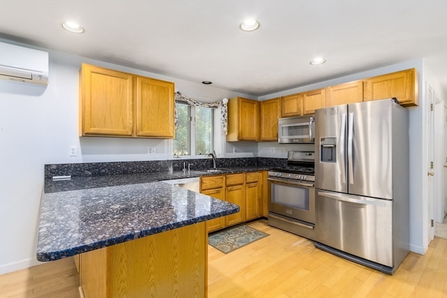 kitchen with an AC wall unit, kitchen peninsula, dark stone counters, light wood-type flooring, and appliances with stainless steel finishes