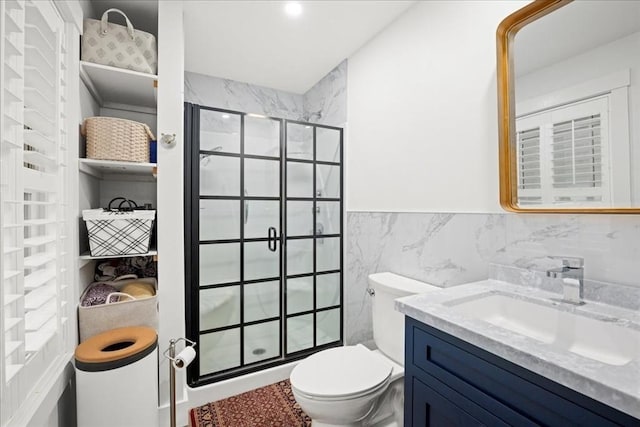 bathroom with a shower with door, vanity, tile walls, and toilet