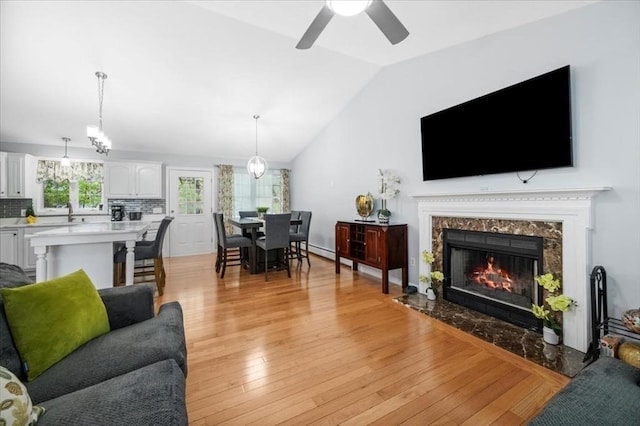 living area with a ceiling fan, light wood-type flooring, lofted ceiling, and a fireplace