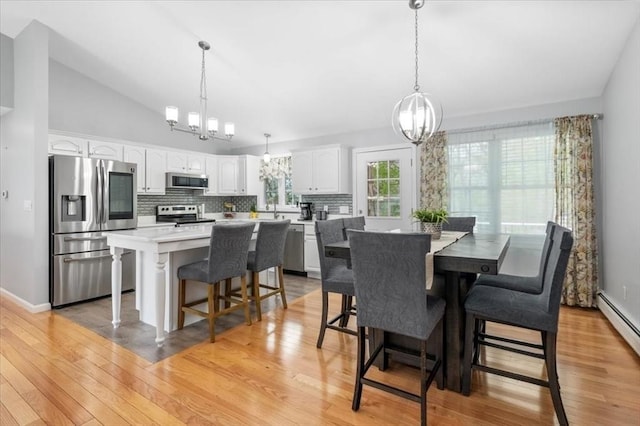 dining space with a chandelier, light wood-style flooring, a baseboard radiator, and baseboards