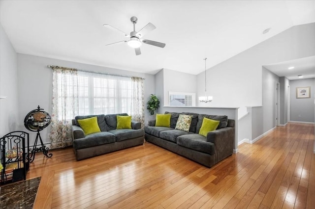 living room featuring lofted ceiling, a chandelier, light wood-type flooring, a ceiling fan, and baseboards