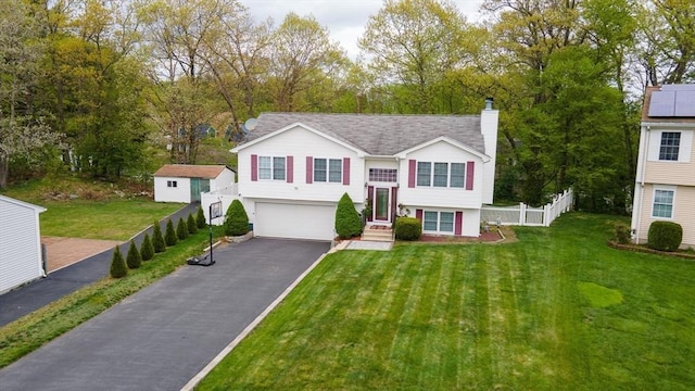 raised ranch featuring driveway, a chimney, an attached garage, and view of wooded area