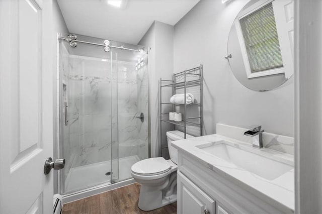 full bath with toilet, wood finished floors, a marble finish shower, vanity, and a baseboard heating unit