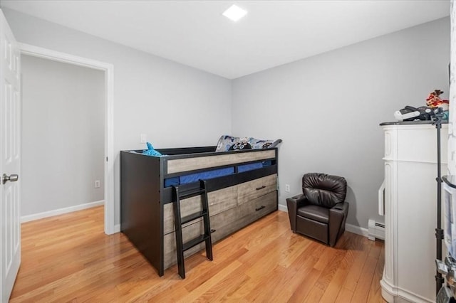 bedroom with light wood finished floors, a baseboard radiator, and baseboards
