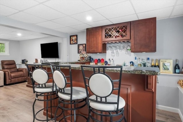 indoor dry bar featuring a drop ceiling, light wood-type flooring, and baseboards
