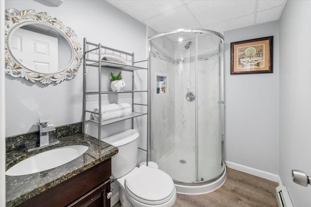 bathroom featuring baseboard heating, wood finished floors, a marble finish shower, toilet, and a drop ceiling