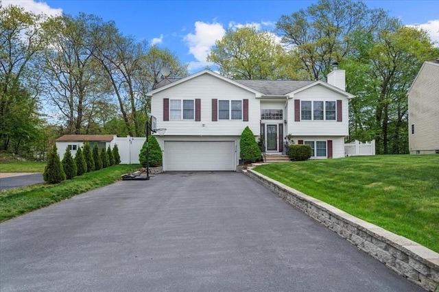 raised ranch featuring an attached garage, a chimney, and asphalt driveway