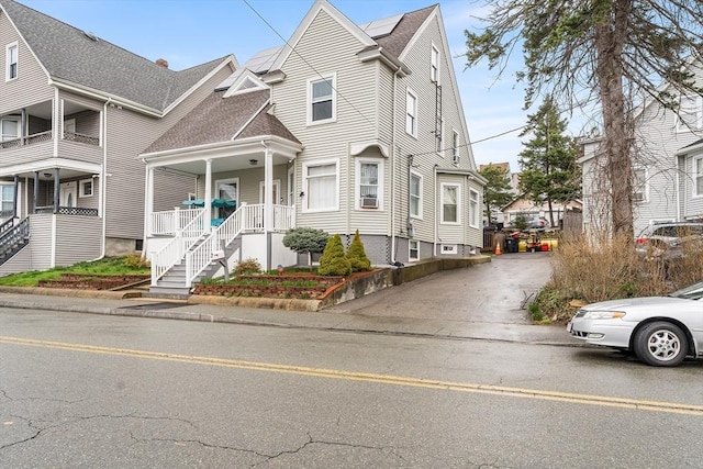 multi unit property featuring roof with shingles, a porch, and roof mounted solar panels