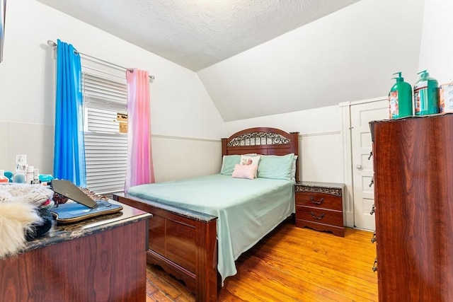 bedroom with light wood finished floors, vaulted ceiling, and a textured ceiling