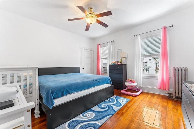 bedroom with a ceiling fan, radiator, wood-type flooring, and multiple windows