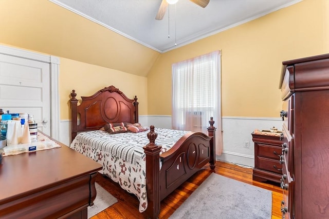 bedroom with a wainscoted wall, wood finished floors, ceiling fan, and vaulted ceiling