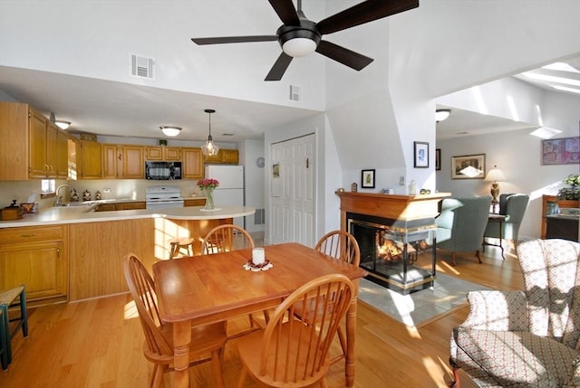 dining space featuring sink, light hardwood / wood-style floors, ceiling fan, and a multi sided fireplace