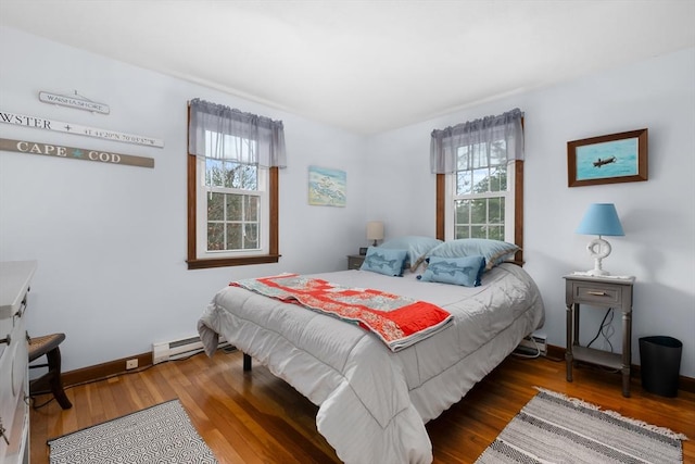 bedroom featuring baseboard heating, wood finished floors, baseboards, and multiple windows