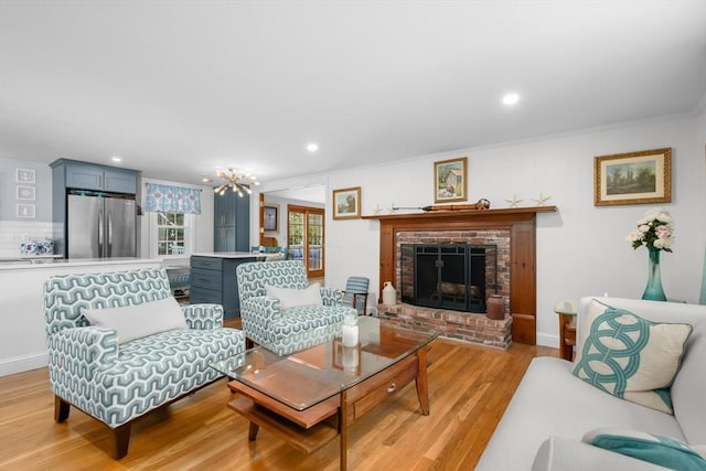 living room with a notable chandelier, a brick fireplace, ornamental molding, recessed lighting, and light wood-style flooring