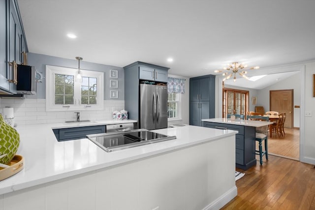 kitchen with a sink, a peninsula, freestanding refrigerator, dark wood finished floors, and blue cabinets