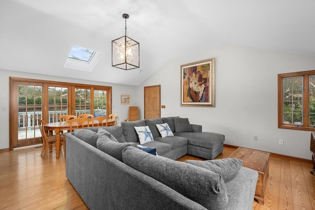 living room featuring light wood-style flooring, an inviting chandelier, baseboards, and lofted ceiling with skylight