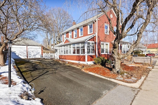 view of front of house with aphalt driveway, a chimney, a sunroom, fence, and an outdoor structure