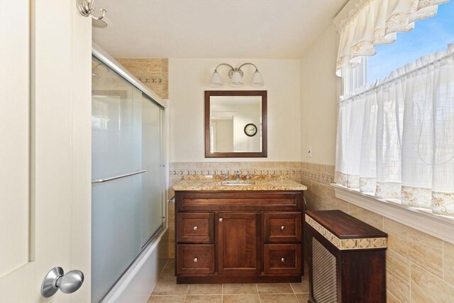 bathroom featuring a wainscoted wall, shower / bath combination with glass door, tile walls, vanity, and tile patterned flooring