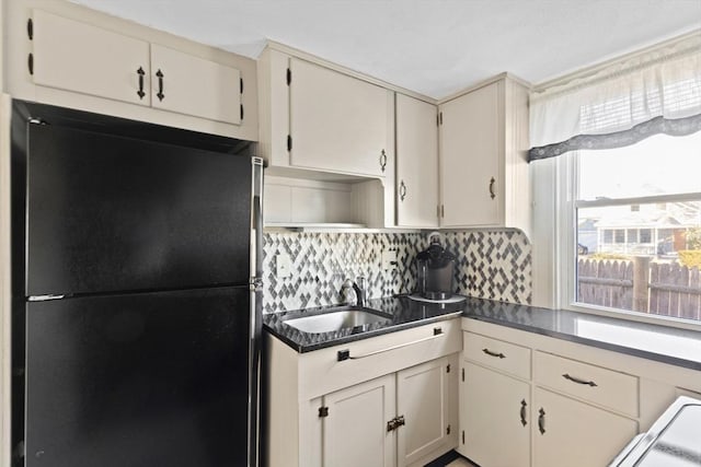 kitchen with tasteful backsplash, dark countertops, freestanding refrigerator, open shelves, and a sink