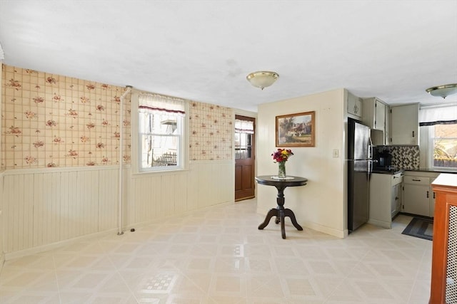 kitchen featuring a wainscoted wall, gray cabinetry, light floors, and freestanding refrigerator