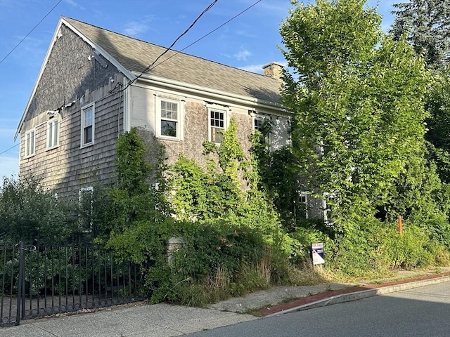 view of home's exterior featuring a shingled roof, fence, and a chimney