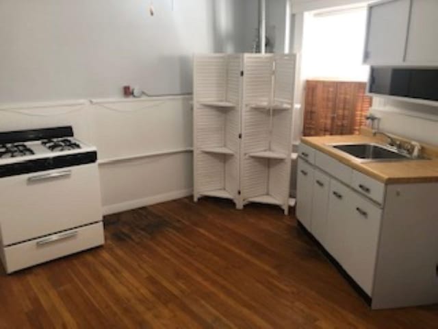 kitchen featuring dark wood-style floors, white range with gas cooktop, a sink, light countertops, and white cabinetry