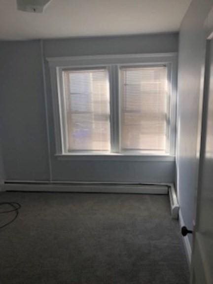 carpeted empty room featuring a baseboard heating unit