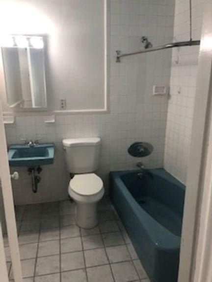 bathroom featuring tile patterned floors, toilet, tile walls, and a sink