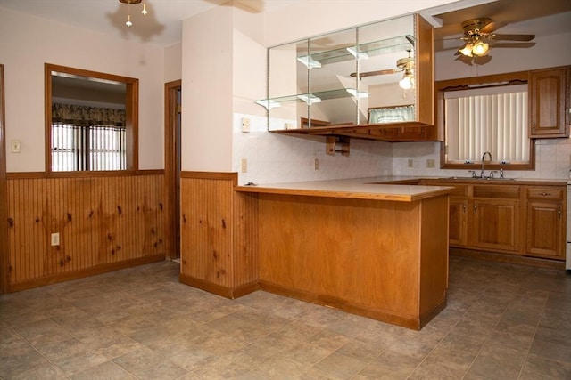 kitchen featuring ceiling fan, wooden walls, kitchen peninsula, and sink